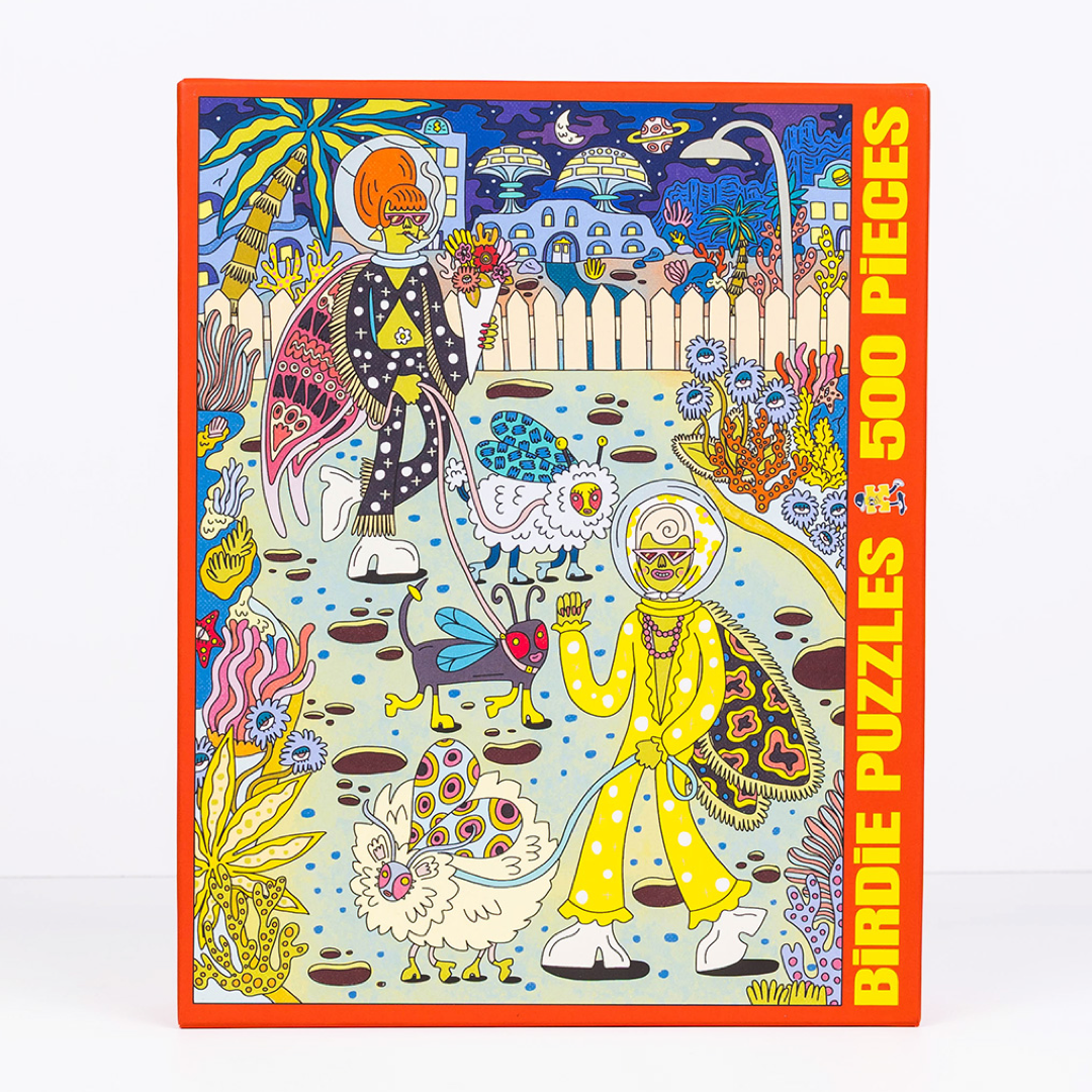 A 500-piece jigsaw puzzle box featuring a highly detailed, colorful psychedelic illustration of two figures in space suits walking in a surreal landscape. The box has a bright orange border and bold yellow text on the right side that reads 'BIRDIE PUZZLES 500 PIECES'.