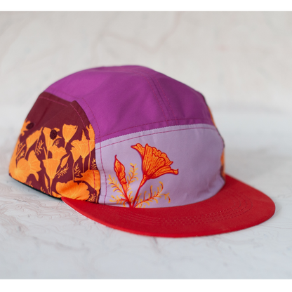 5 panel hat with a red brim and different shades of purple on each panel. Hat features poppy artwork