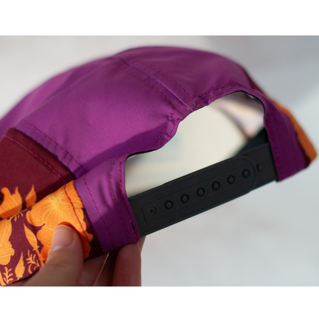 Close-up of a purple and orange cap with a black strap held by a hand on a light gray background