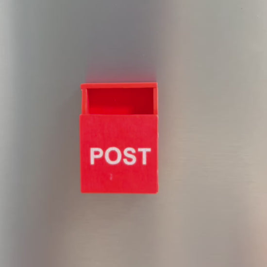 A video showing a small post box on a fridge. A post it note then comes into frame and a hand folds the post it and puts it into the box. The hand takes the post box off the fridge to show the magnet on the back 