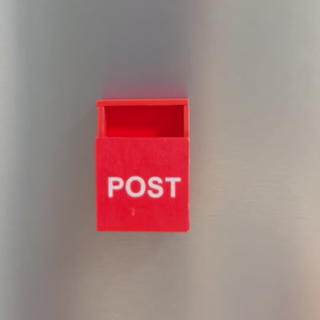 A video showing a small post box on a fridge. A post it note then comes into frame and a hand folds the post it and puts it into the box. The hand takes the post box off the fridge to show the magnet on the back 
