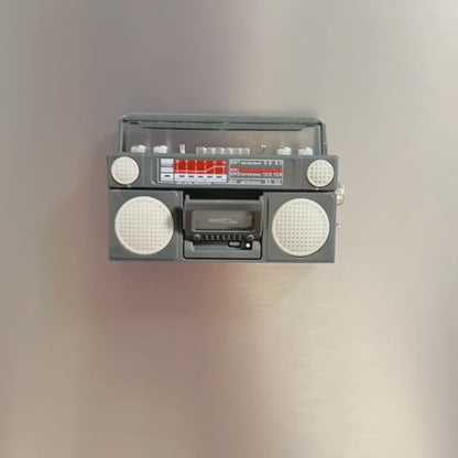 Video showing retro-style boombox-shaped refrigerator magnet on a fridge. A hand then reaches info frame to put a tape in the boombox then picks it up off the fridge to show the magnet on the back