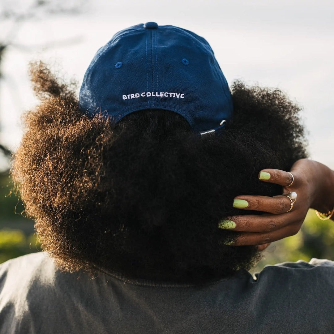 Person wearing a blue cap with 'BIRD COLLECTIVE' logo, standing outdoors.