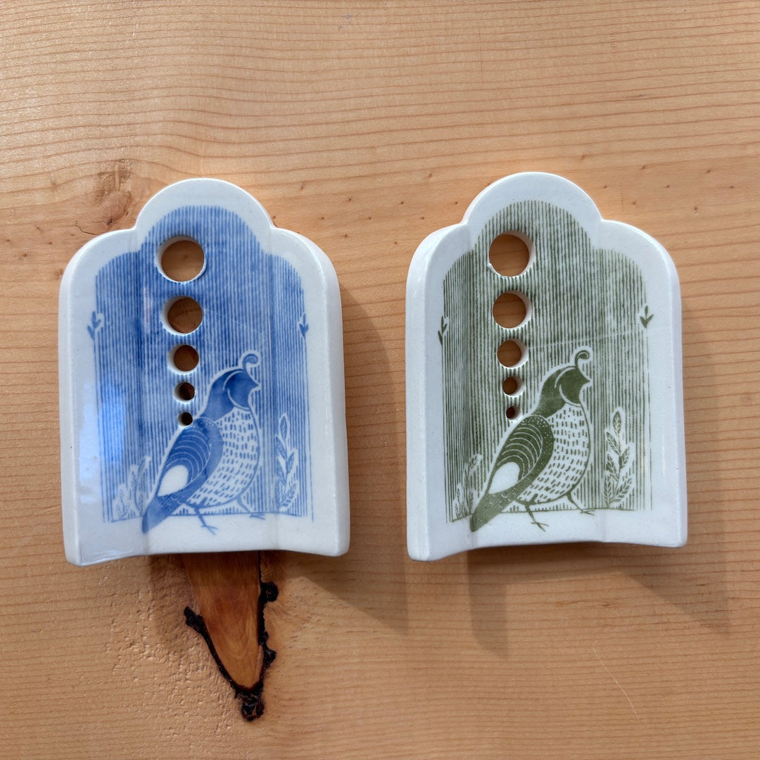 2 ceramic herb strippers. Both have 5 different sized holes to pull herbs through to remove the leaves. The one on the left has blue stripes and a quail at the bottom, the one on the right has green stripes and a quail on the bottom.
