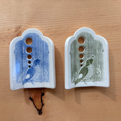 2 ceramic herb strippers. Both have 5 different sized holes to pull herbs through to remove the leaves. The one on the left has blue stripes and a quail at the bottom, the one on the right has green stripes and a quail on the bottom.