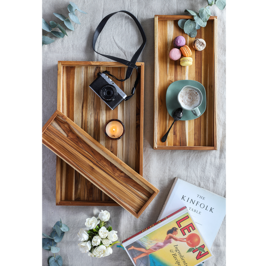 Wooden trays with a camera, mug, and other items on a textured surface.