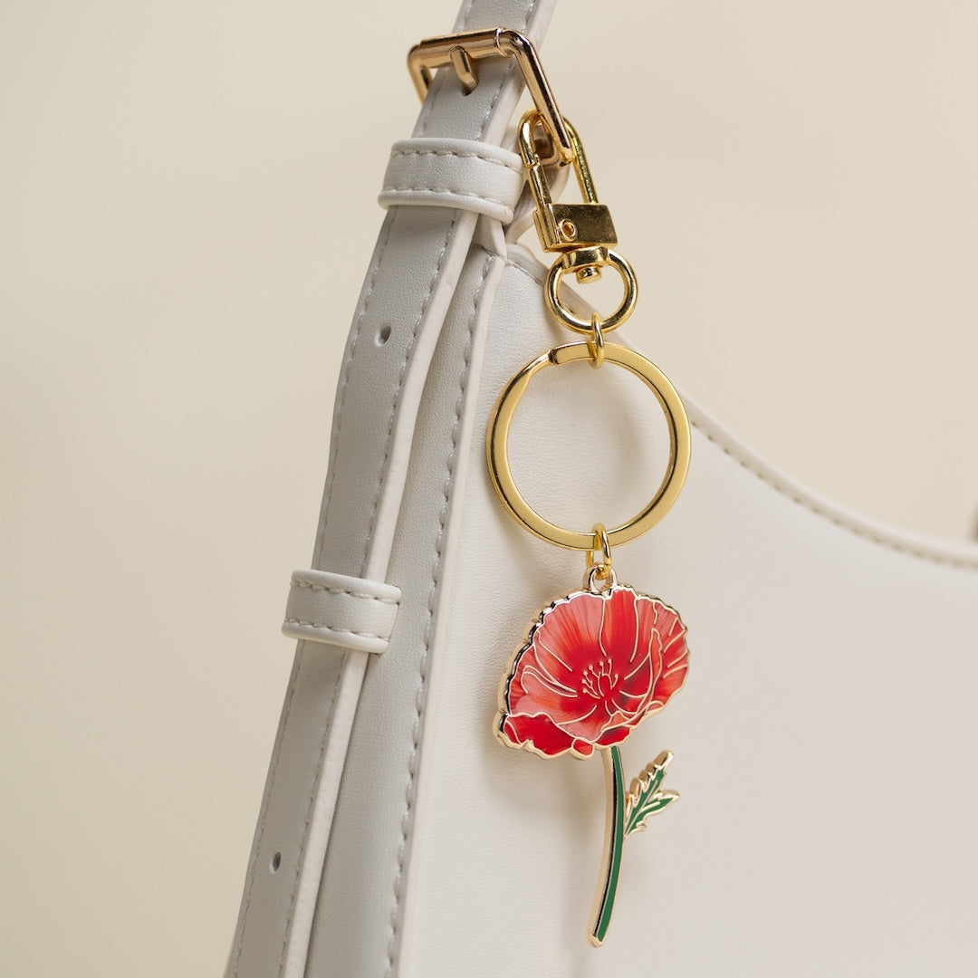 Keychain with a red poppy charm attached to a purse strap on a light background