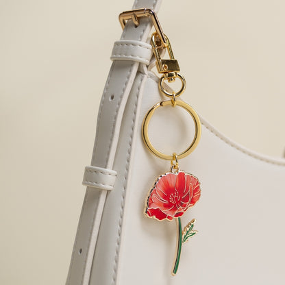 Keychain with a red poppy charm attached to a purse strap on a light background