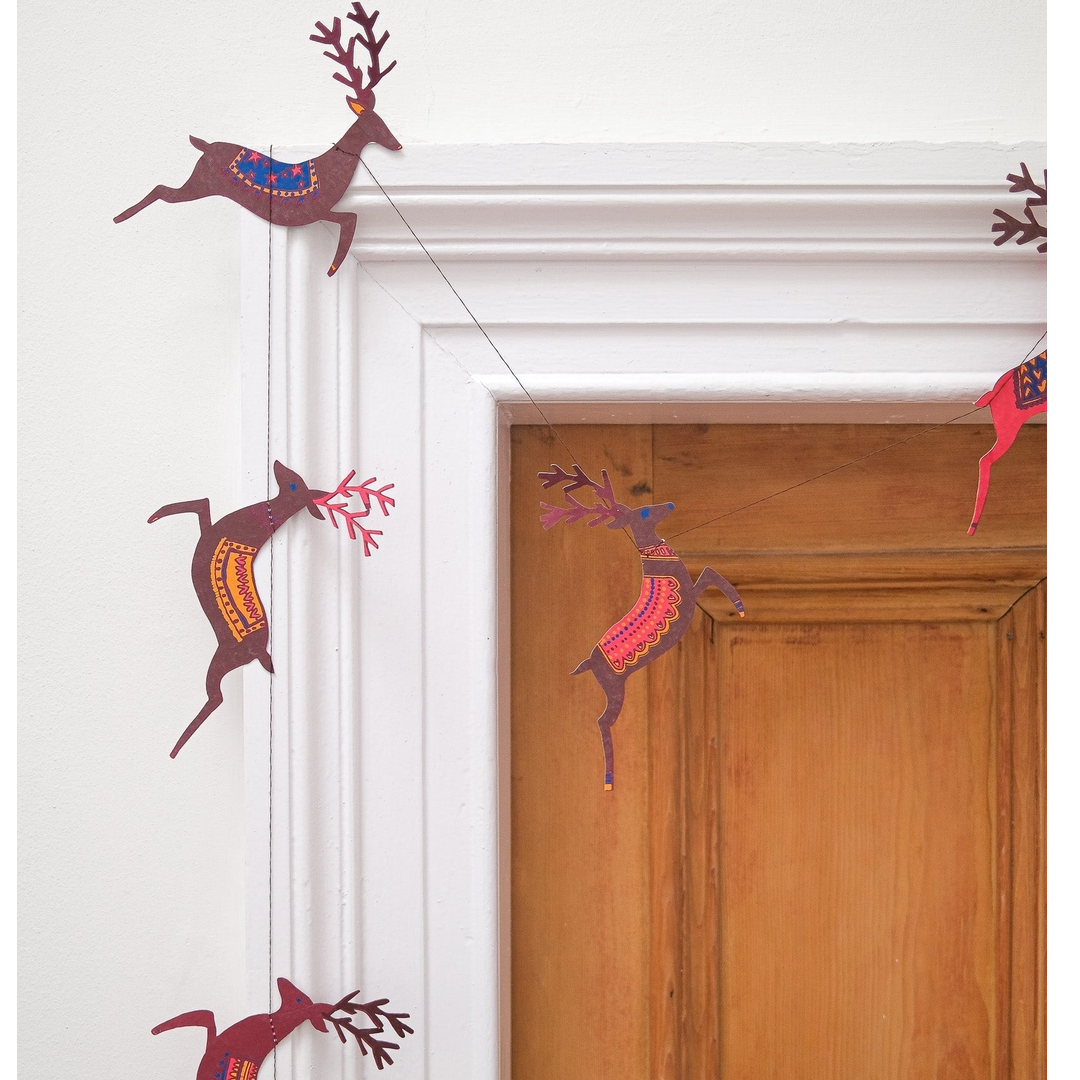 A string of hanging paper reindeer garland in brown, red, and orange tones, displayed on a white door frame next to a wooden door.