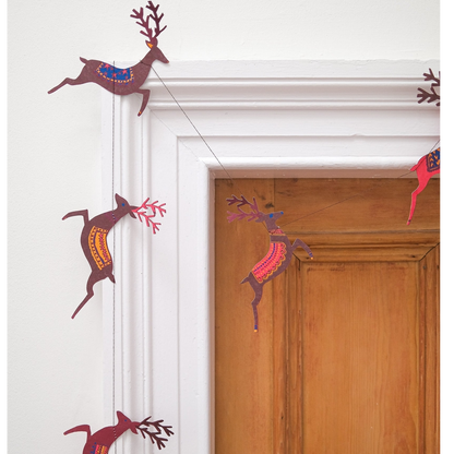A string of hanging paper reindeer garland in brown, red, and orange tones, displayed on a white door frame next to a wooden door.