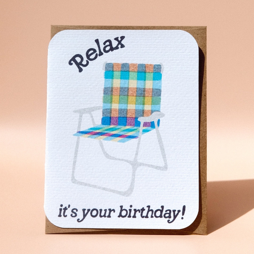 Greeting card with a rainbow lawn chair that has text that reads relax it's your birthday 