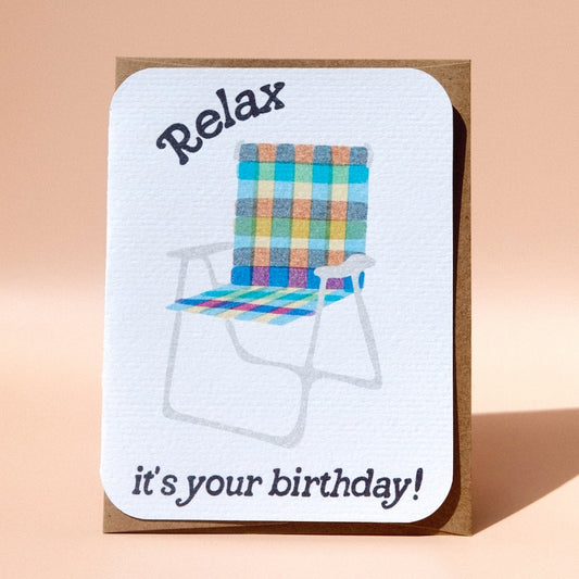 Greeting card with a rainbow lawn chair that has text that reads relax it's your birthday 