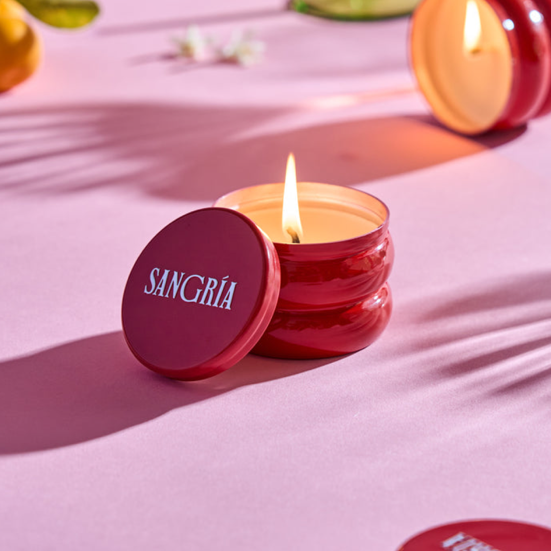 Red candle labeled 'Sangria' on a pink surface with decorative elements.