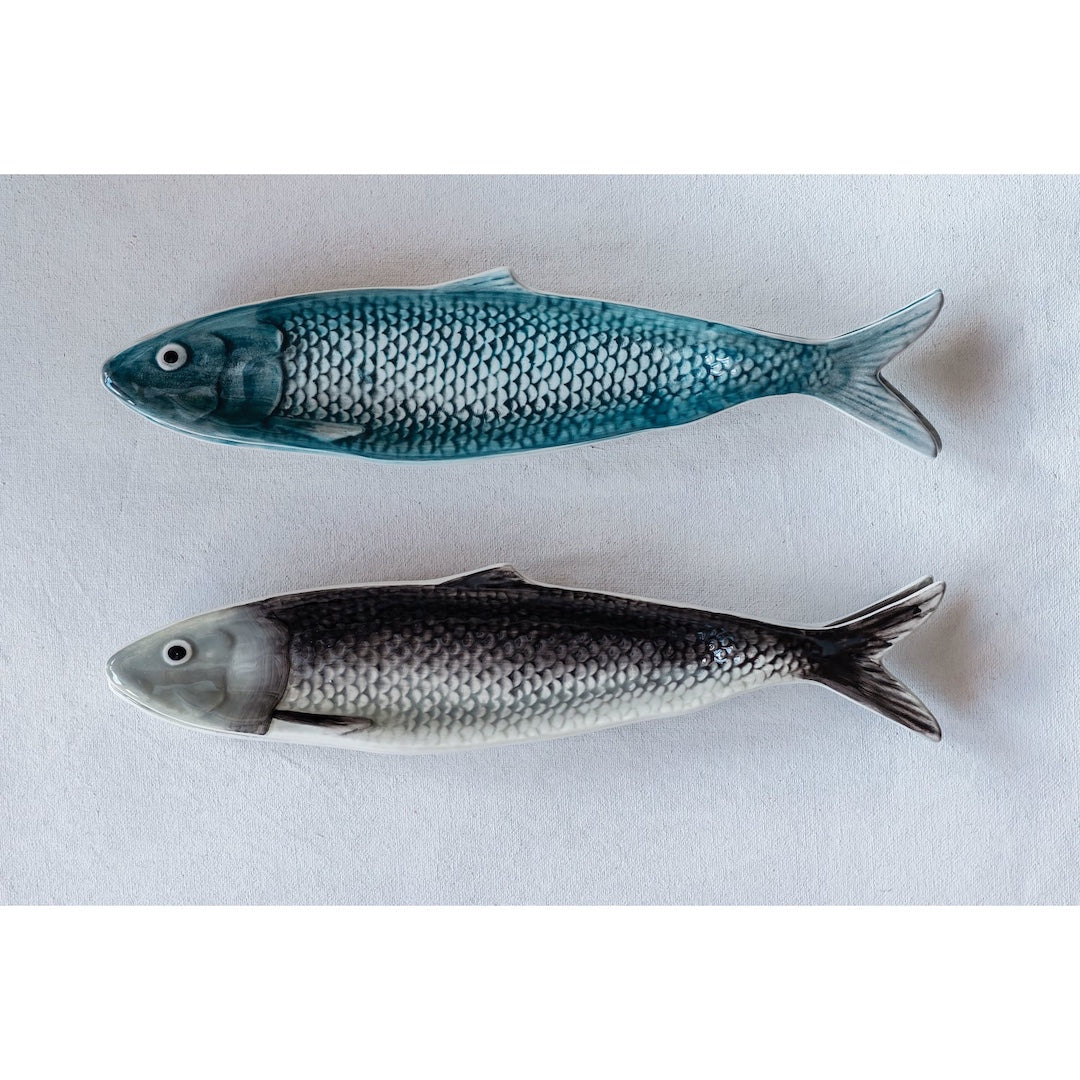 Two sardine shaped plates, one blue and one gray, on a white background