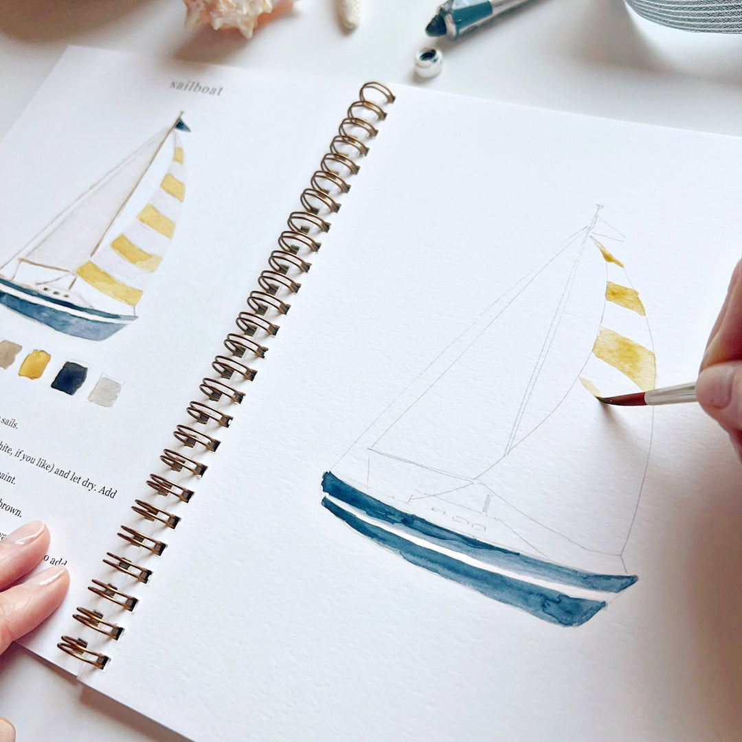 Person painting a sailboat illustration in a notebook with watercolors.