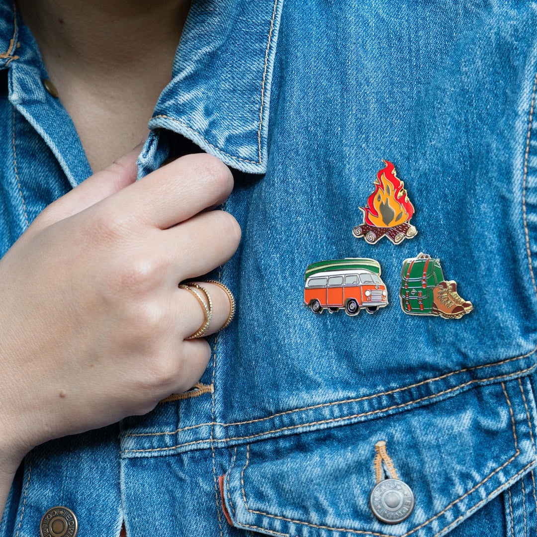 Person wearing a denim jacket with camping-themed pins.