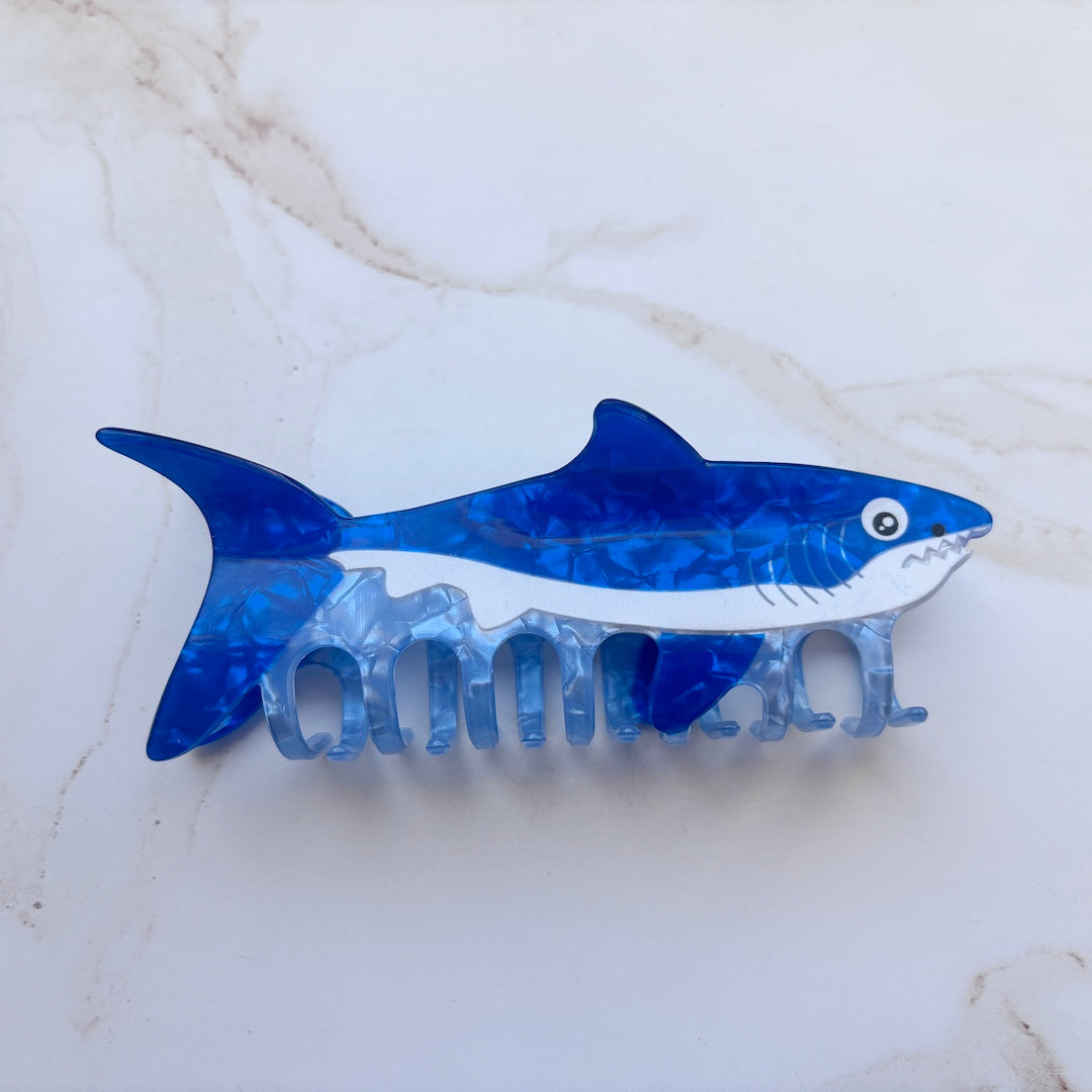 Blue shark-shaped hair clip on a marble background