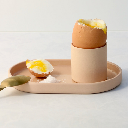 Egg cup with cracked egg on a peach tray on a light background