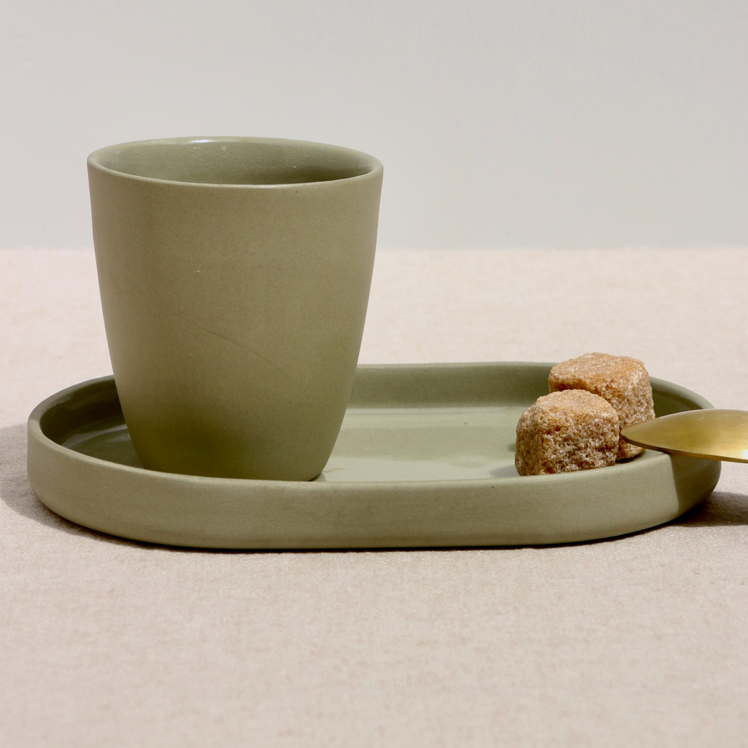 Sage green ceramic cup on an oval shaped tray with sugar cubes on a beige surface