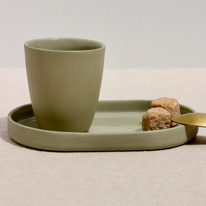 Sage green ceramic cup on an oval shaped tray with sugar cubes on a beige surface