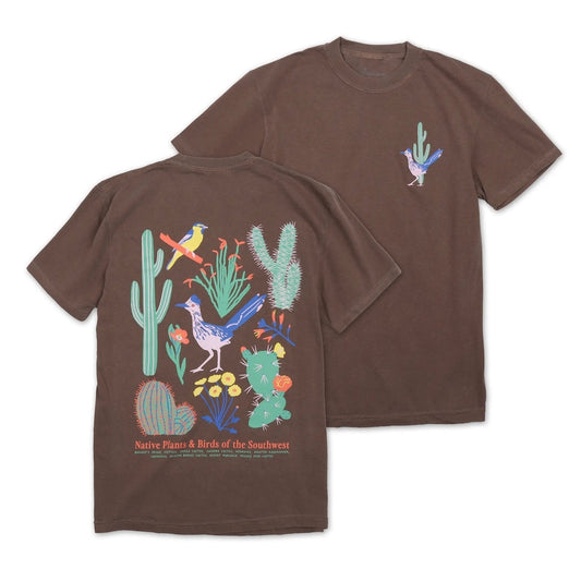 Two brown short-sleeve T-shirts shown on a white background, with the front and back views overlapping. The back shirt features a large colorful desert illustration with cacti, birds, and text reading 'Native Plants & Birds of the Southwest.