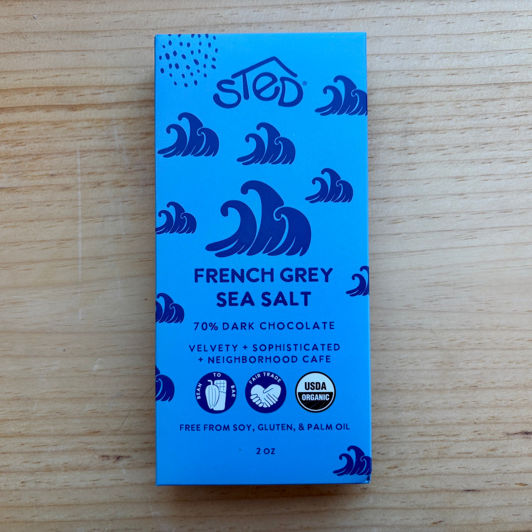 A blue chocolate bar package labeled 'sted' and 'French Grey Sea Salt' with dark blue wave illustrations, photographed on a light wood surface.
