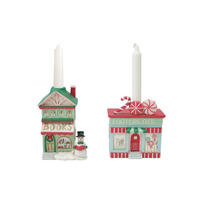 Two small holiday-themed candle holders shaped like storefronts, one labeled "BOOKS" with a snowman figure, and one labeled "CANDY LAND CAFE" with candy cane decorations, on a plain white background.