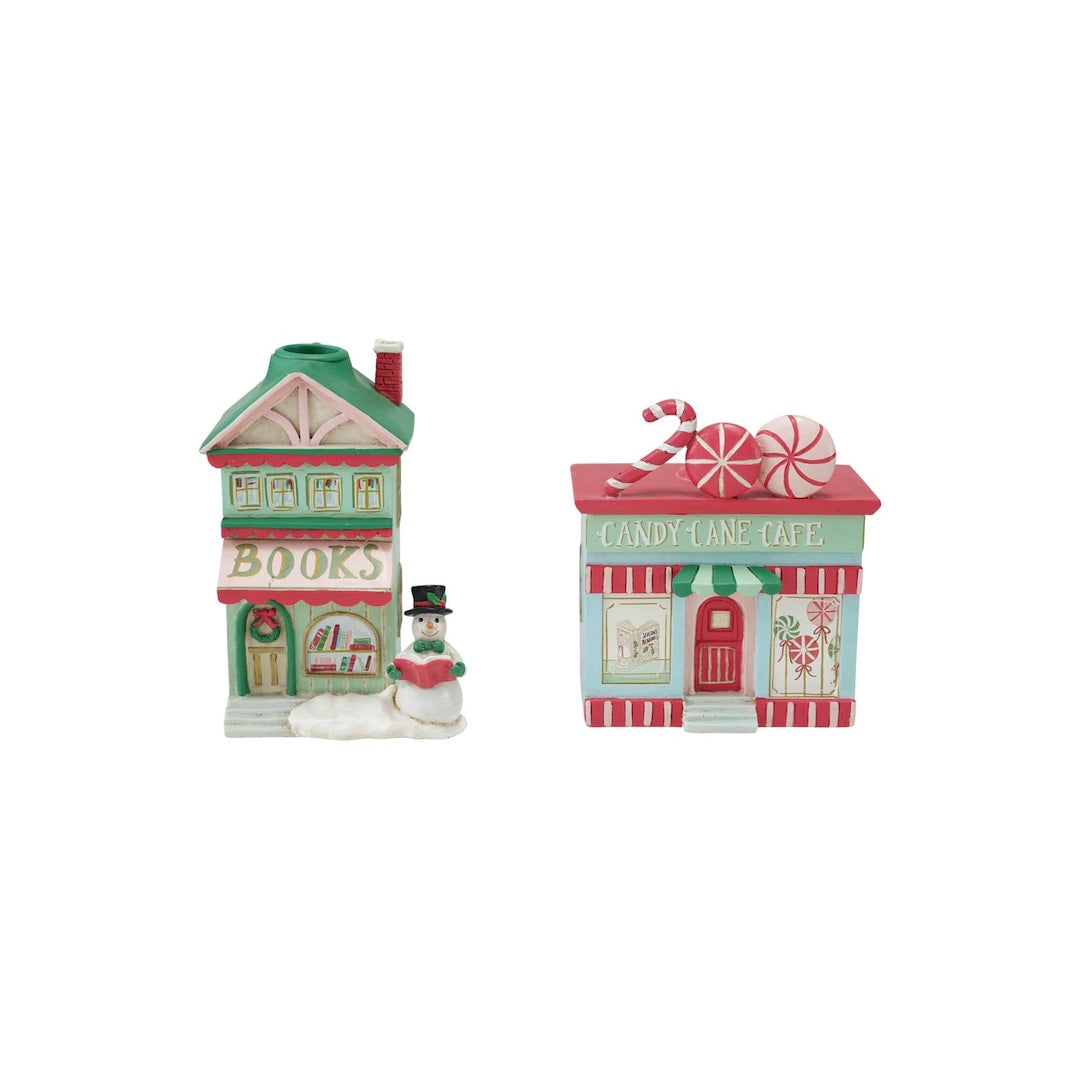 Two small holiday-themed candle holders shaped like storefronts, one labeled "BOOKS" with a snowman figure, and one labeled "CANDY LAND CAFE" with candy cane decorations, on a plain white background.