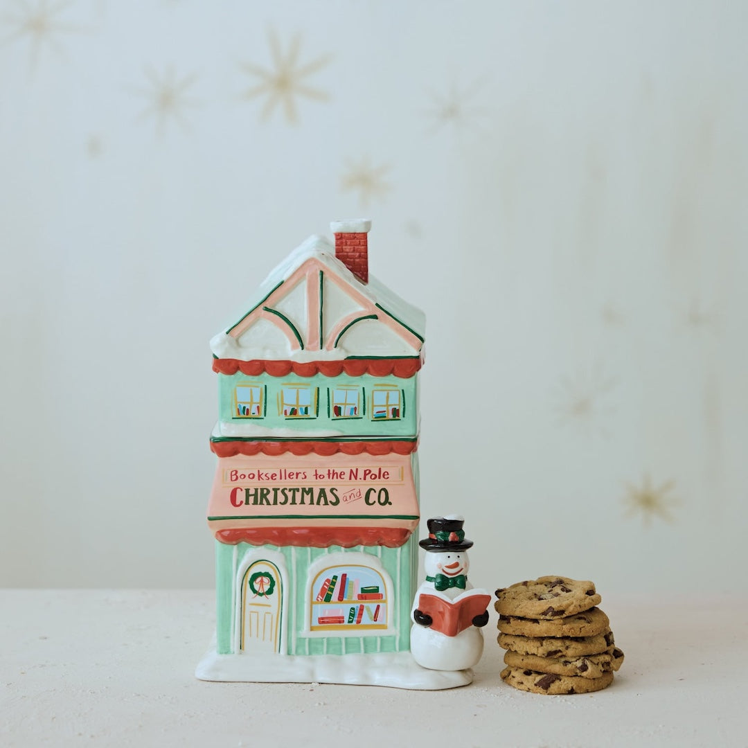 Decorative house-shaped cookie jar with a snowman and cookies on a light background