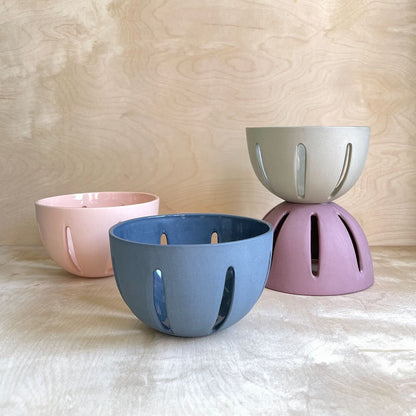 Four ceramic berry bowls in pink, blue, and purple on a wooden surface.