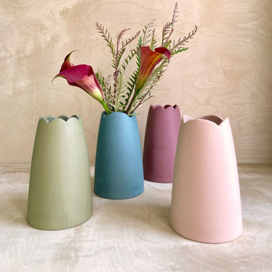 Four ceramic vases in different colors with flowers on a light background