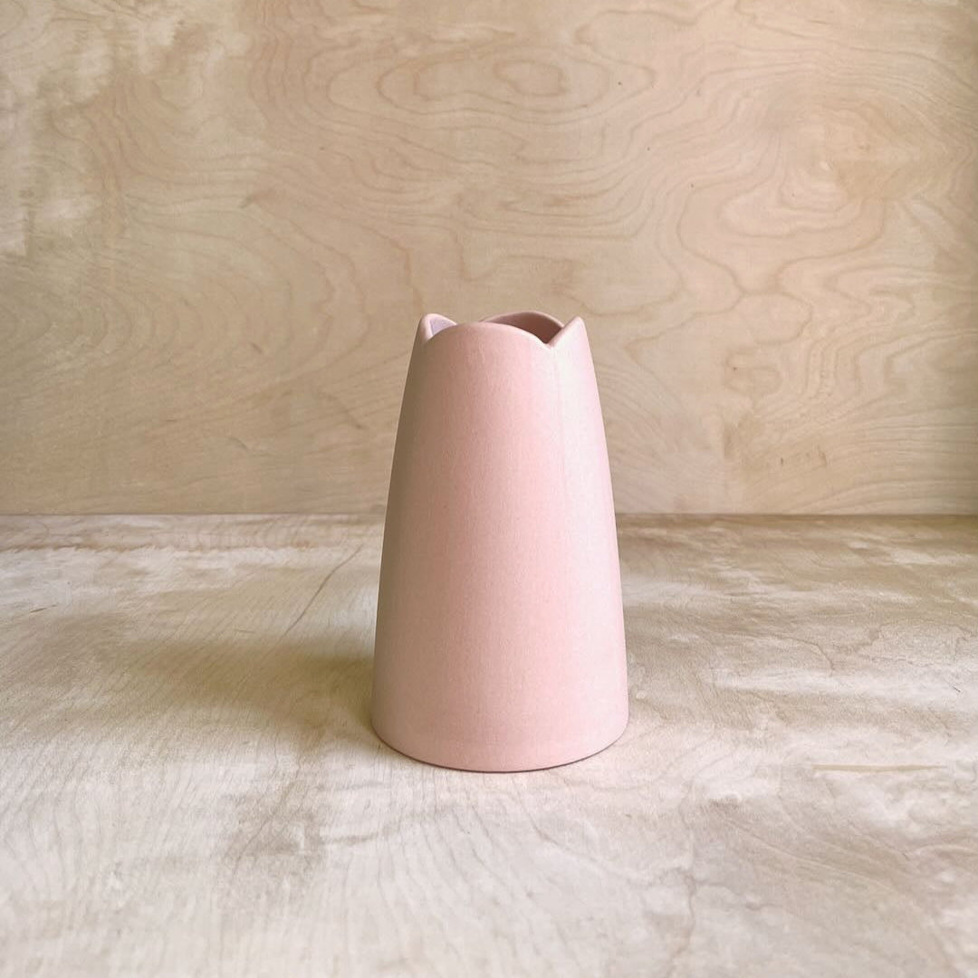 Pink ceramic vase on a wooden surface with a wooden background