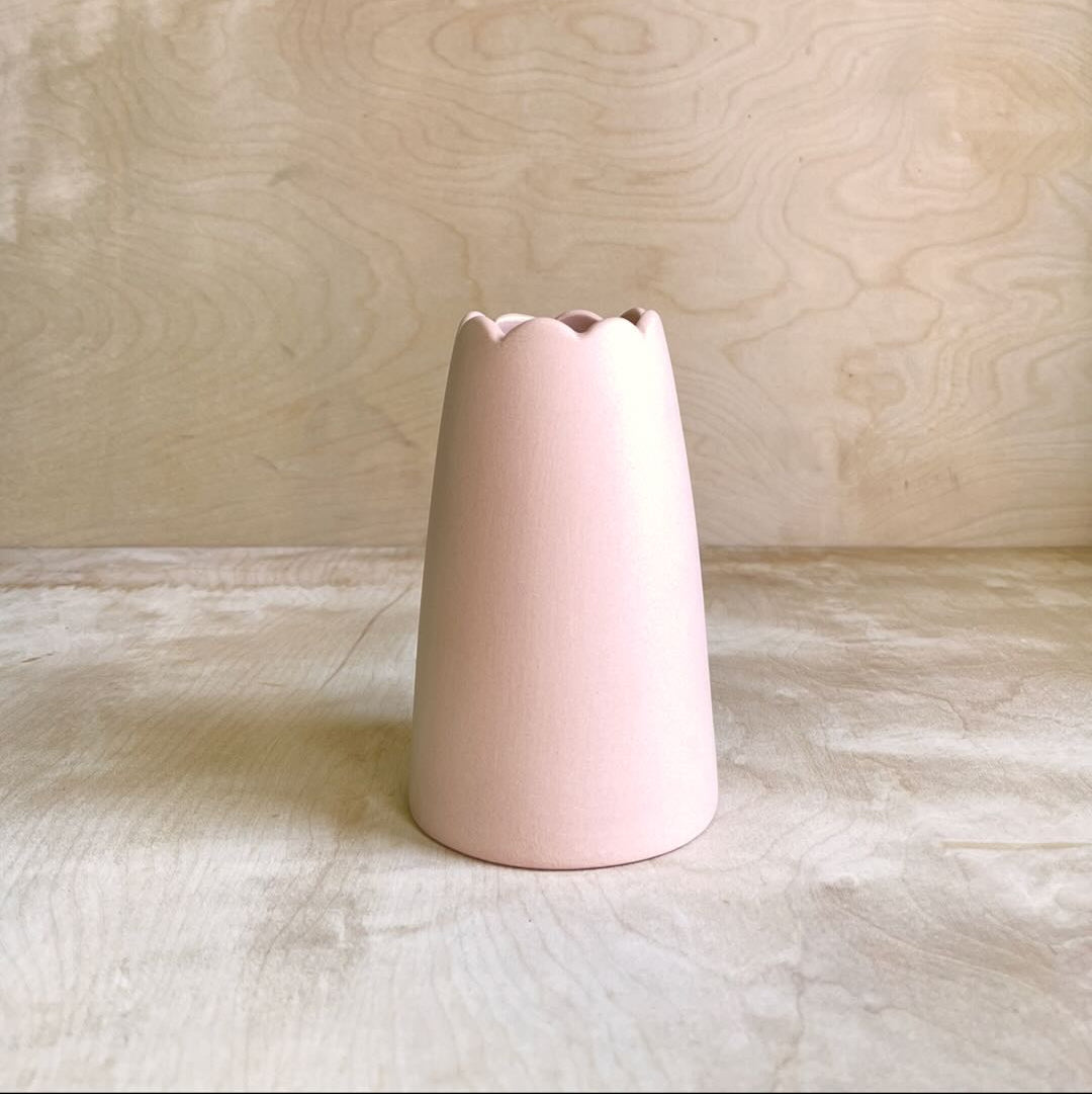 Pink ceramic vase on a light wooden surface with a wooden background