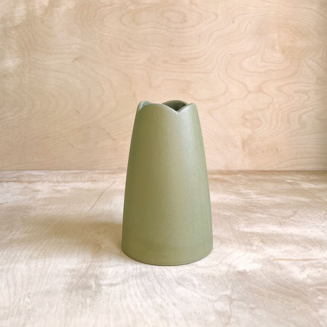 Green ceramic vase on a light wooden surface with a light wood panel background