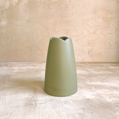 Green ceramic vase on a light wooden surface with a light wood panel background