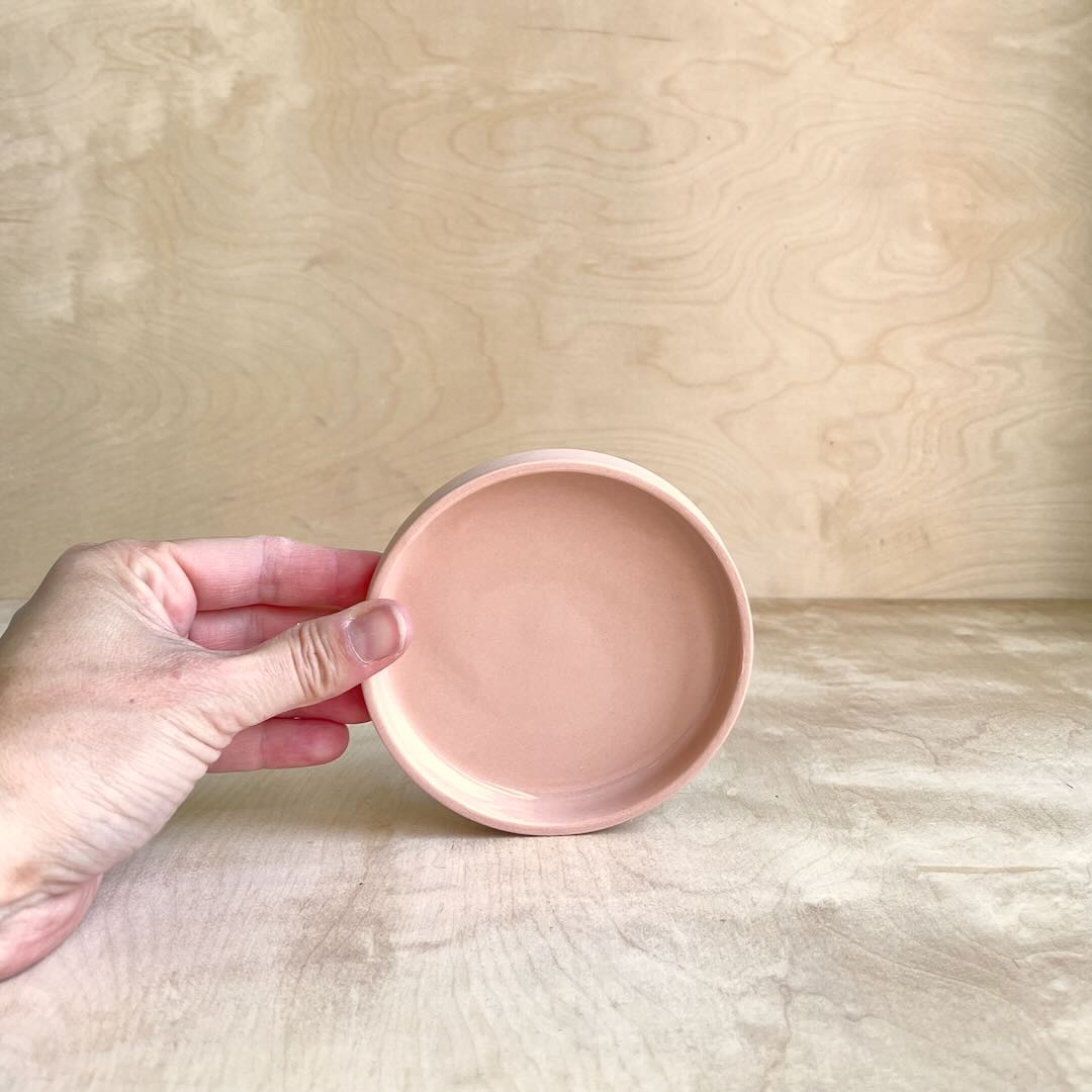 Hand holding a small round pink ceramic dish against a wooden background