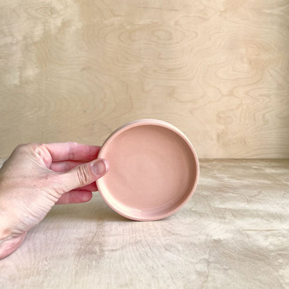 Hand holding a small round pink ceramic dish against a wooden background