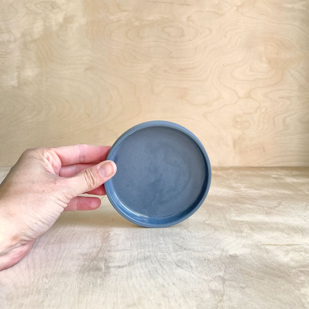 Hand holding a small round blue ceramic dish against a wooden background