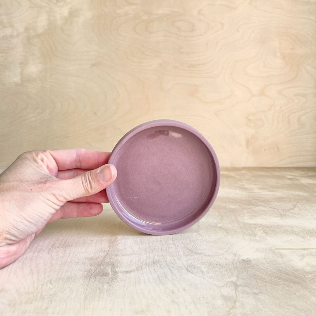 Hand holding a small round purple ceramic dish against a wooden background