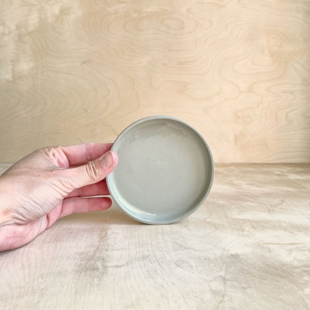 Hand holding a small light green ceramic dish against a wooden background