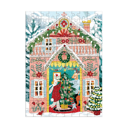 A colorful Christmas village scene jigsaw puzzle featuring a decorated pink house with snow on the roof, a Christmas tree at the center door, a reindeer, a fox, and other festive animals in a snowy outdoor setting.