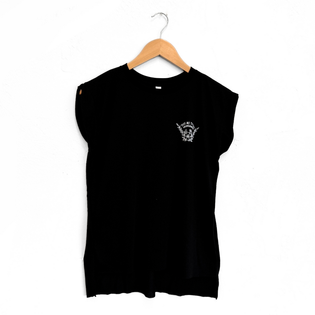 Black sleeveless shirt on a hanger against a white background. The shirt has a small white logo that says take me to the wildflowers 