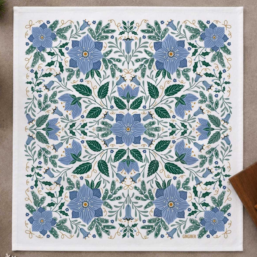 Towel featuring a symmetrical botanical pattern with blue flowers, green leaves, and delicate gold vine details, laid flat on a neutral surface.