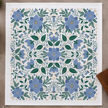 Towel featuring a symmetrical botanical pattern with blue flowers, green leaves, and delicate gold vine details, laid flat on a neutral surface.