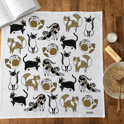 Tea towel with cat pattern on a wooden surface with kitchen items.