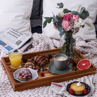 Wooden tray with breakfast items including coffee, pastries, and fruit on a cozy blanket.
