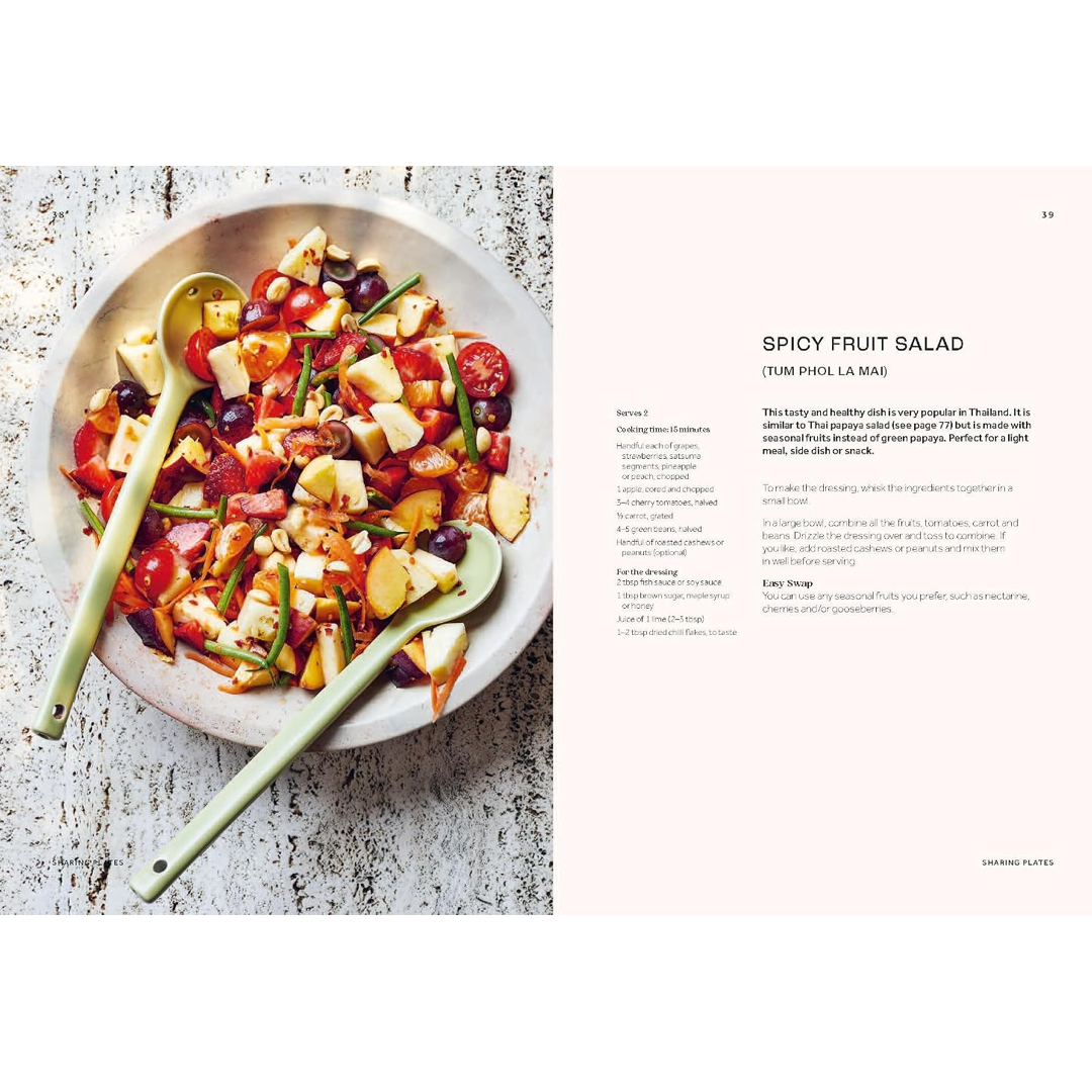 A printed recipe spread page showing a prepared spicy fruit salad in a bowl on the left and the recipe text for 'Spicy Fruit Salad' on the right, photographed on a light rustic surface.