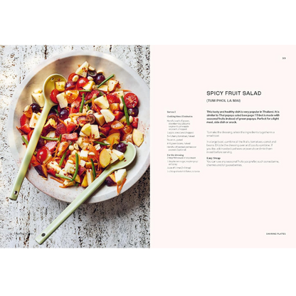 A printed recipe spread page showing a prepared spicy fruit salad in a bowl on the left and the recipe text for 'Spicy Fruit Salad' on the right, photographed on a light rustic surface.