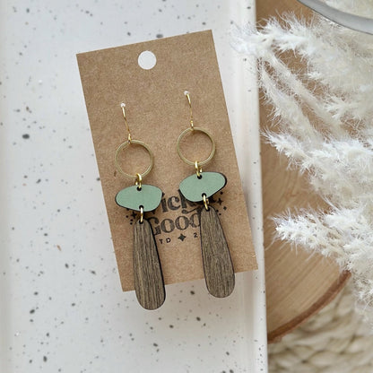 Pair of earrings on a cardboard backing with a textured white background. The earrings are long dangle earrings that are made of wood and meant to resemble a tree