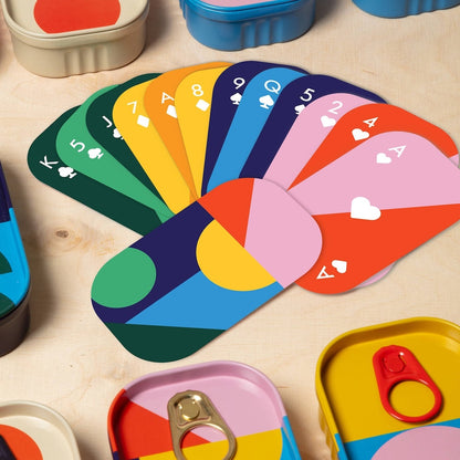 Colorful playing cards fanned out on a wooden surface with toy containers.